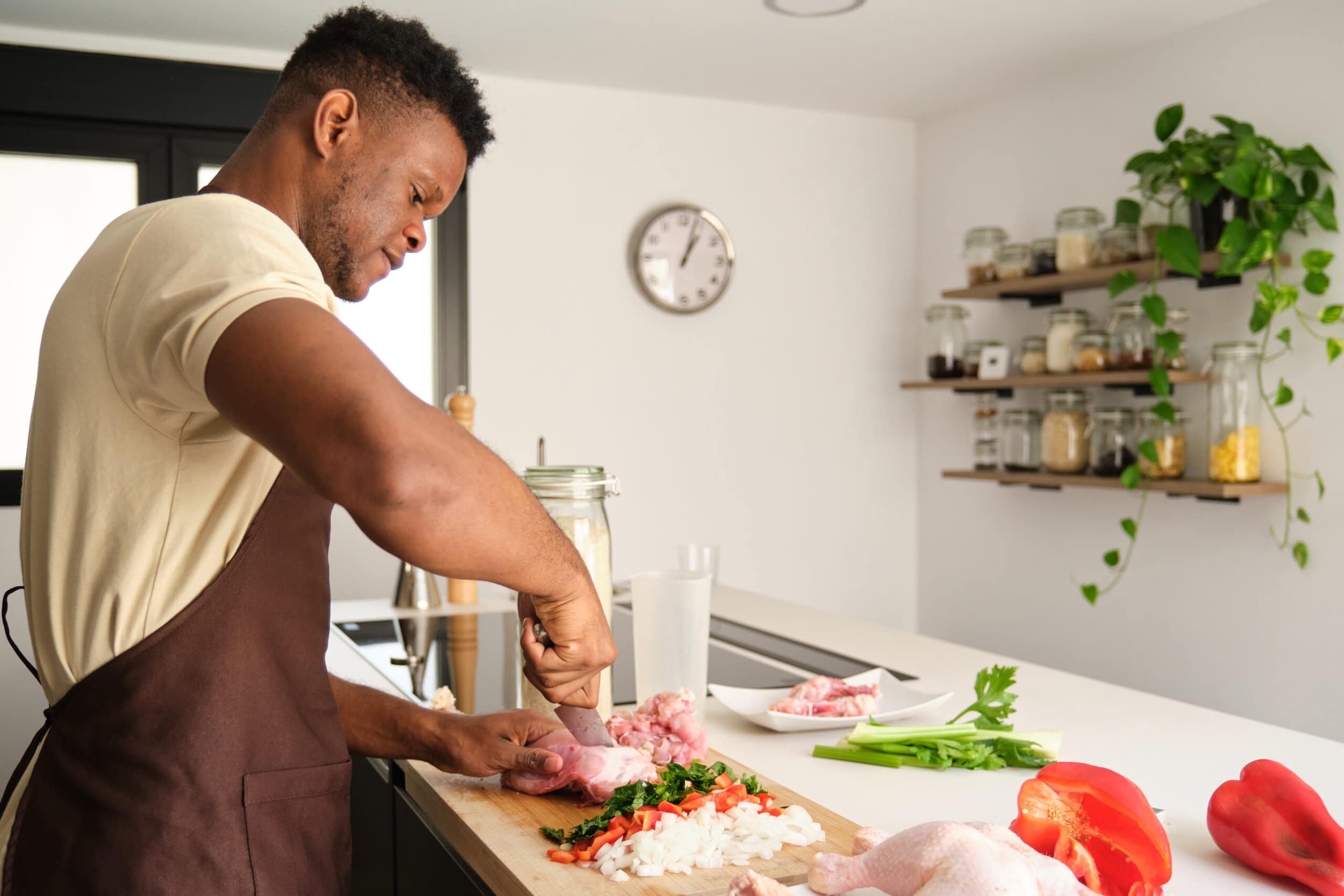 Young black man de-boning chicken to prepare a recipe in a kitchen.